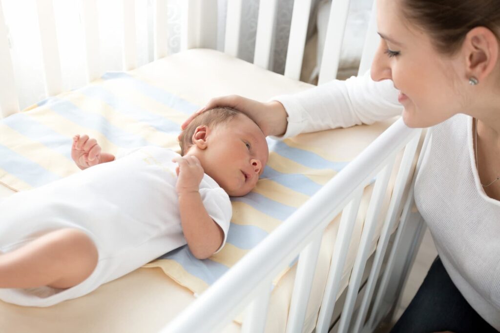 An image of a happy smiling mother caressing her baby lying in cot.