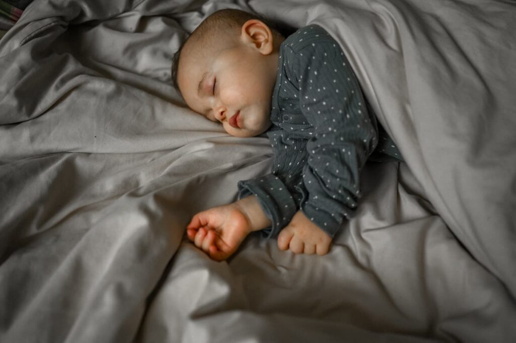 An image of a cute baby sleeping under the blanket at home on the bed.
