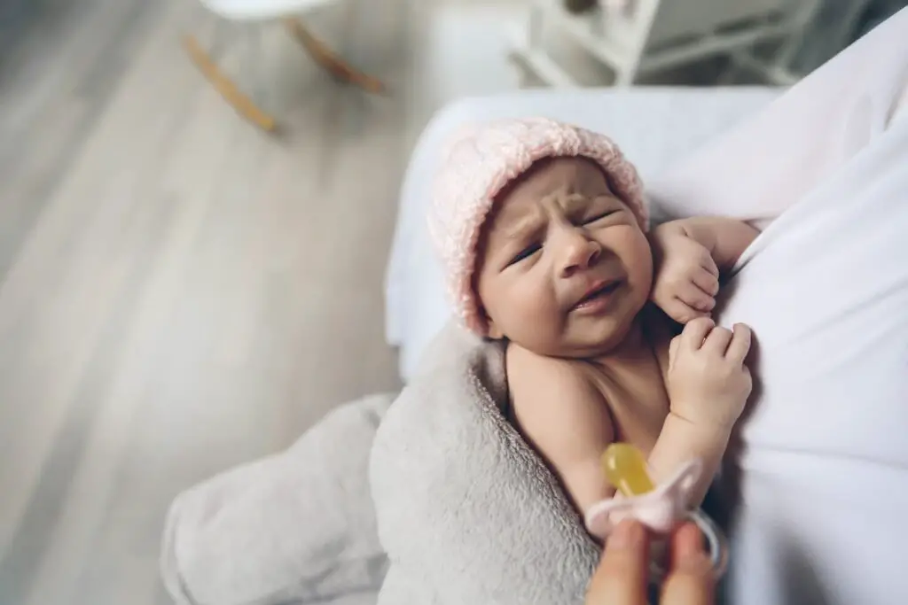 An image of a newborn baby girl crying because she wants the pacifier.