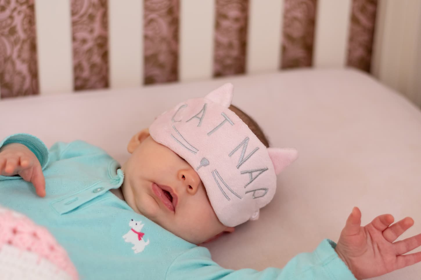 An image of a Baby in a crib wearing a sleep mask that says Cat Nap.