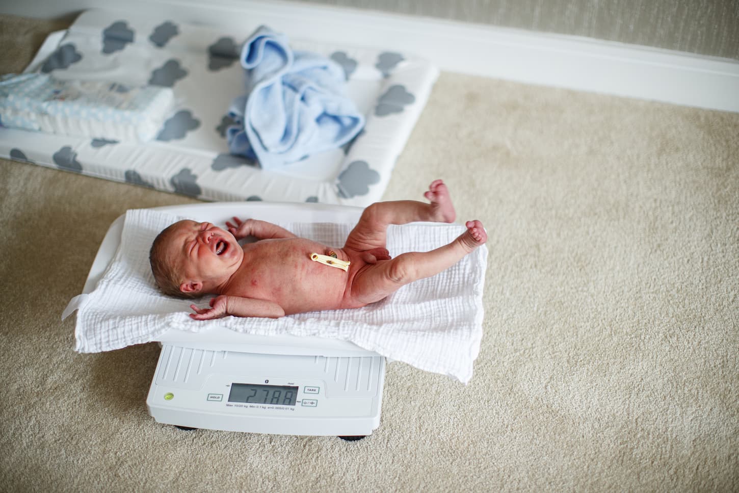 An image of crying newborn baby lying on a weighing scales.