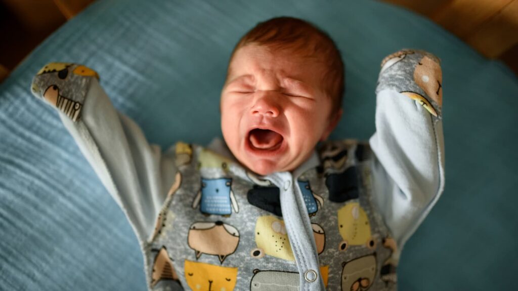 An image of a newborn baby boy crying in his crib.