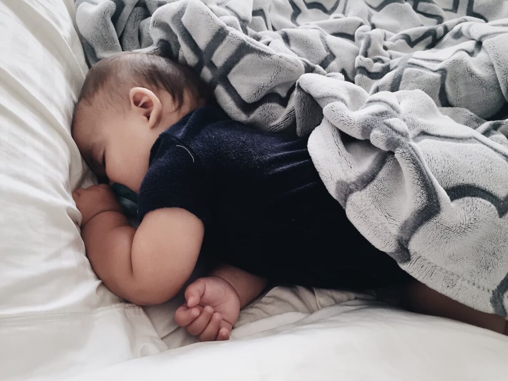 An image of a baby sleeping on a bed during the daytime.