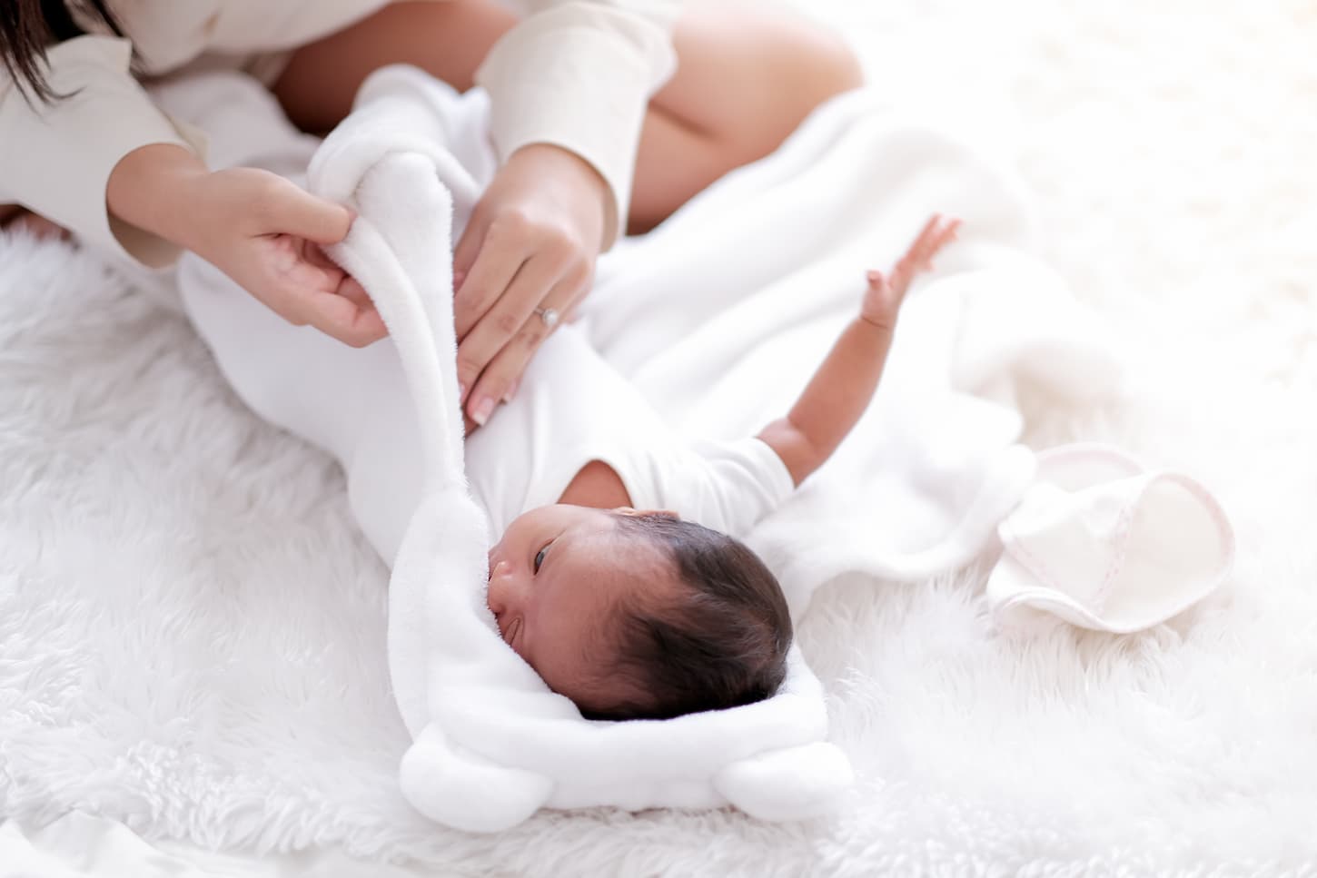An image of a mother while swaddling her newborn baby with a white cloth on the bed.