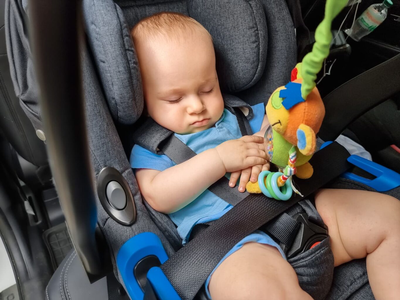 An image of a baby boy sleeping in the safety seat of a car and next to his toy.