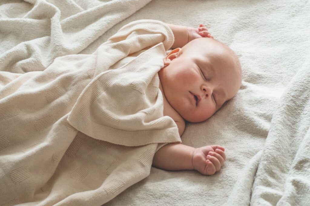 An image of a newborn baby sweetly sleeping on the bed.