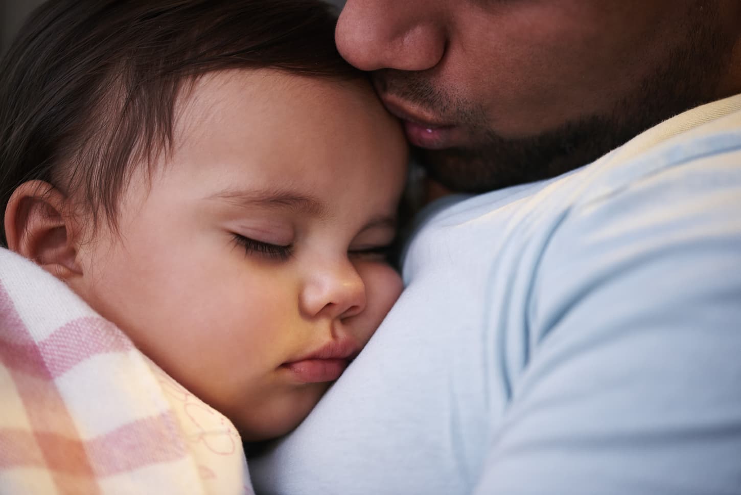 An image of a father kissing his child while sleeping next to his chest.
