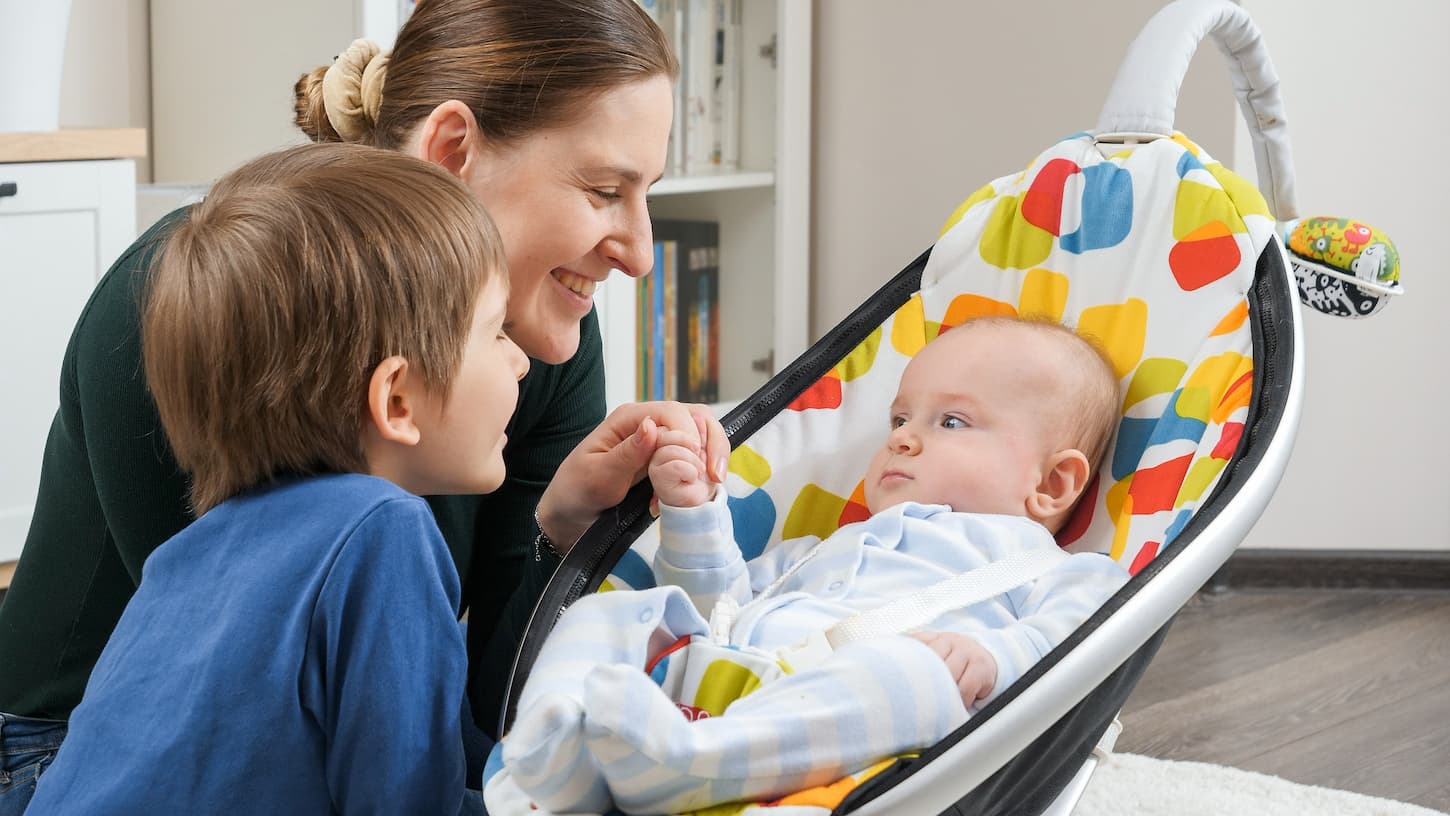 an image of a baby in a mamaroo with mom and sibling looking on