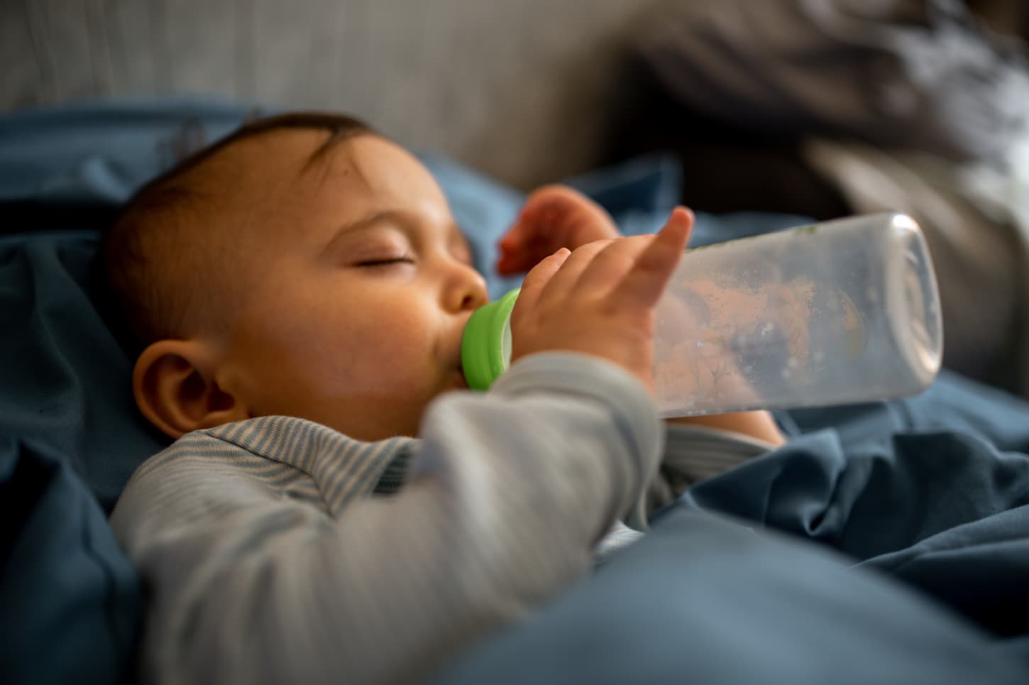 An image of a sleeping baby with a bottle in his hands.