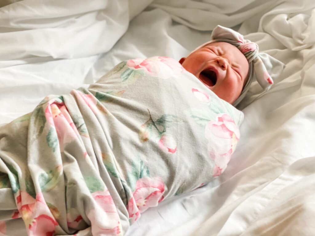 An image of a swaddled newborn baby with mouth wide open yawning or crying.