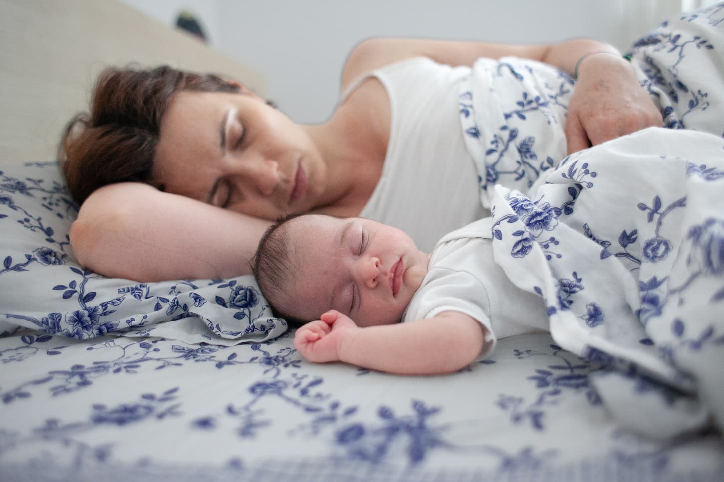An image of a young mother sleeping next to her baby on the bed.