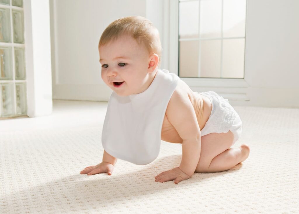 An image of a smiling baby crawling around the house on a white carpeted floor.