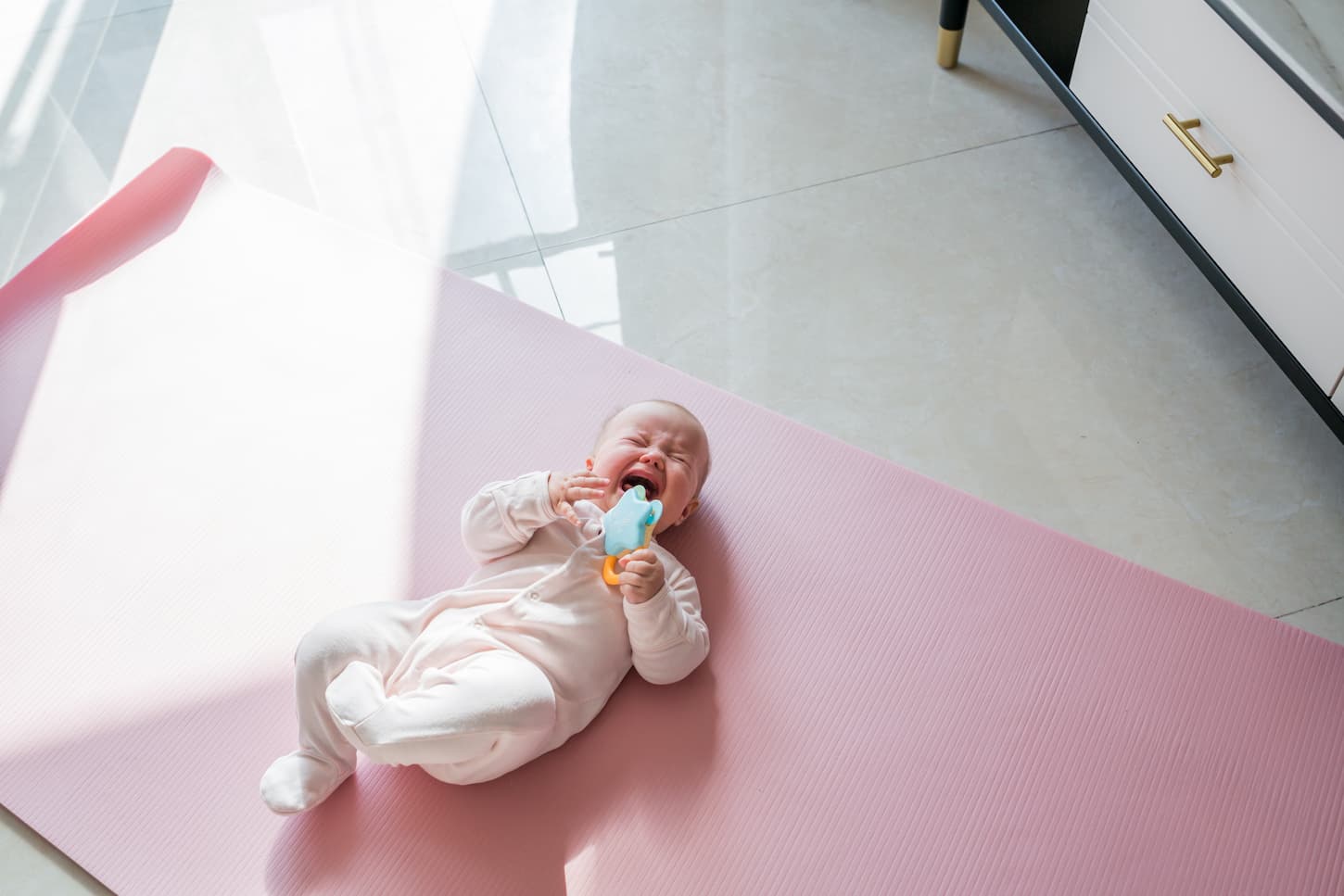 An image of a baby 5-6 months old crying in pain at home on pink mat.