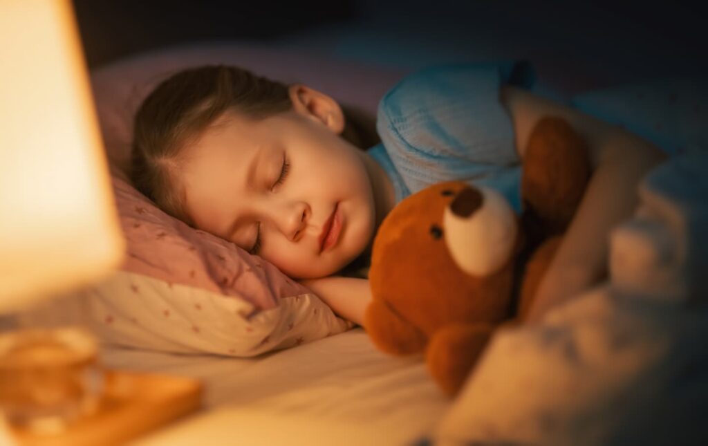 An image of a sleeping adorable little girl hugging her stuffed toy in the bed.