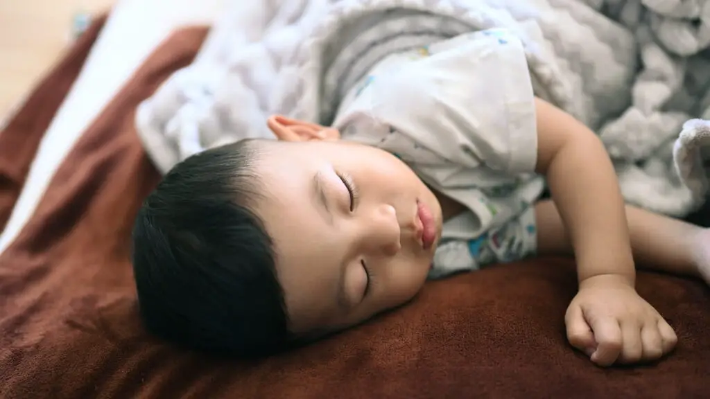An image of of baby boy sleeping on bed at home.