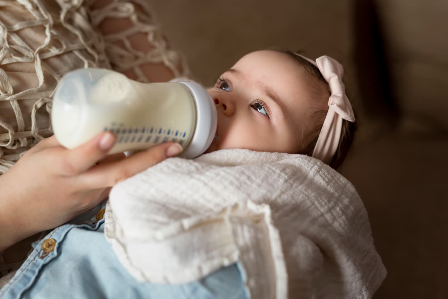 An image of a mother holding her baby girl in her arms and feeding her with breast milk in a bottle.