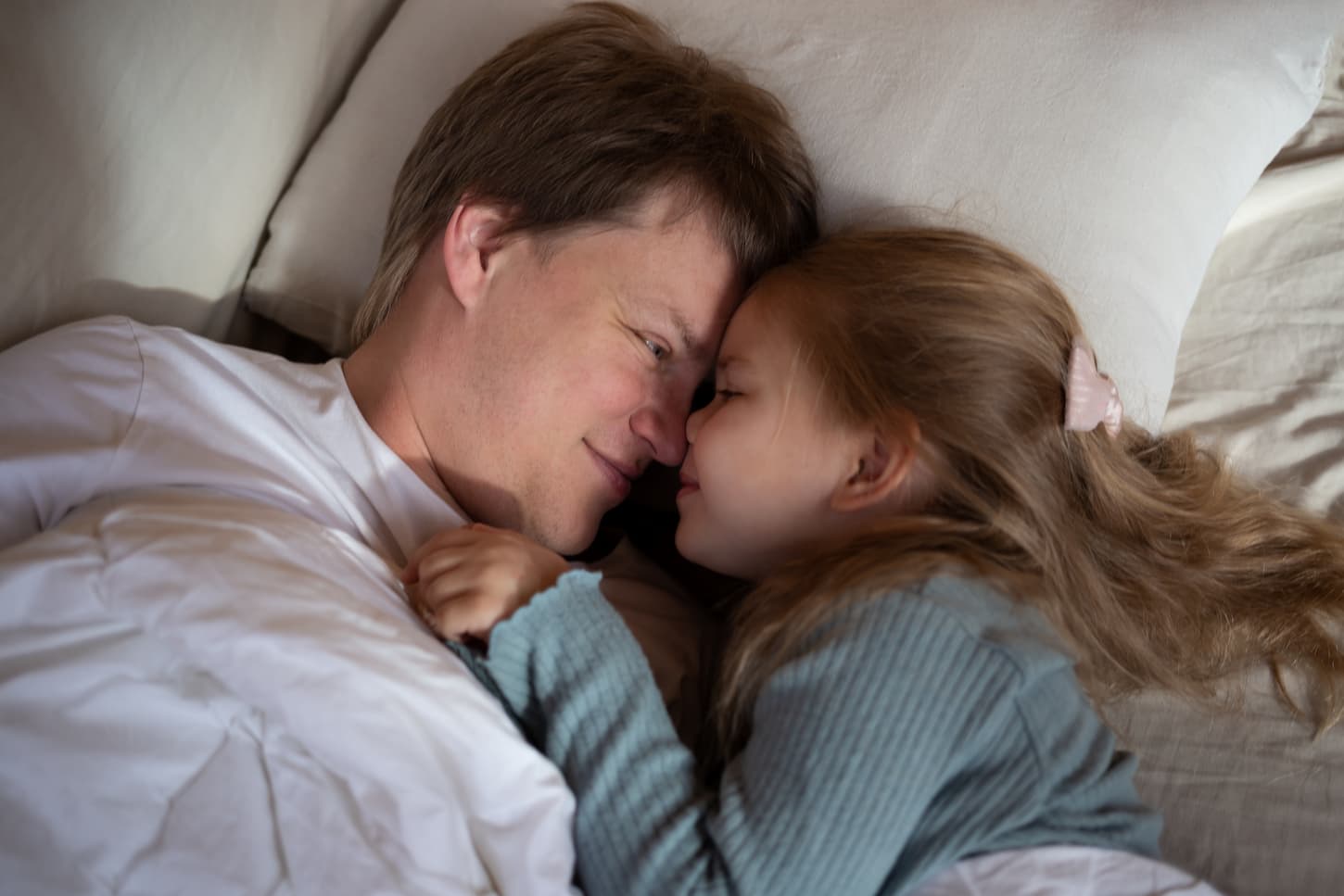 An image of a little cute girl hugging her dad while lying together in bed.