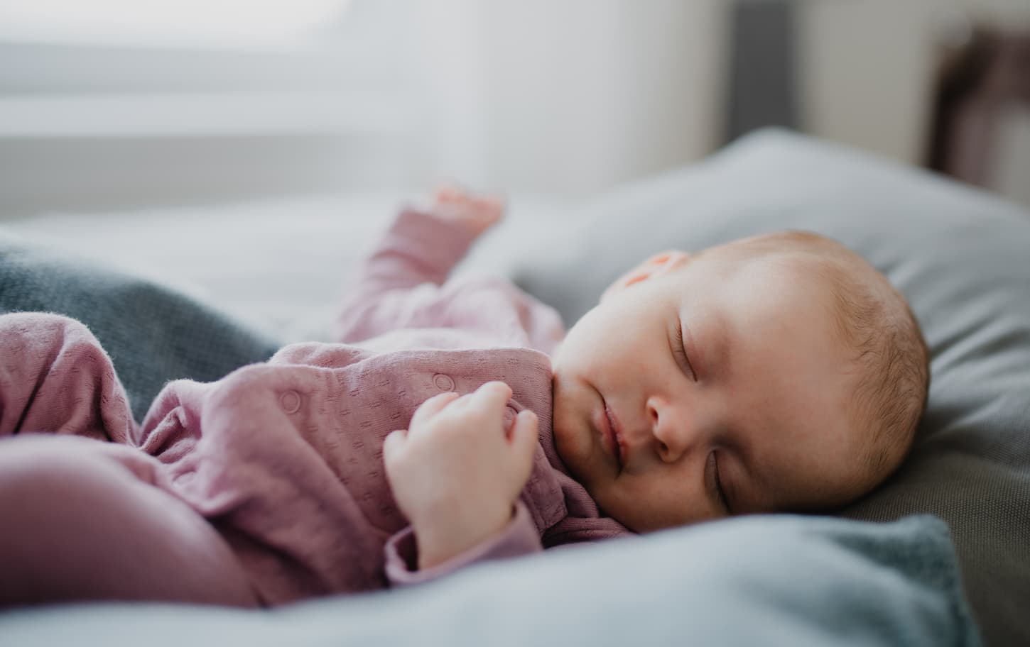 An image of a cute newborn baby girl, sleeping and lying on a sofa indoors at home.
