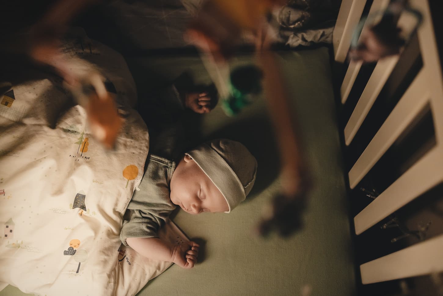 An image of a sleeping baby in a baby cot with mobile over his head.