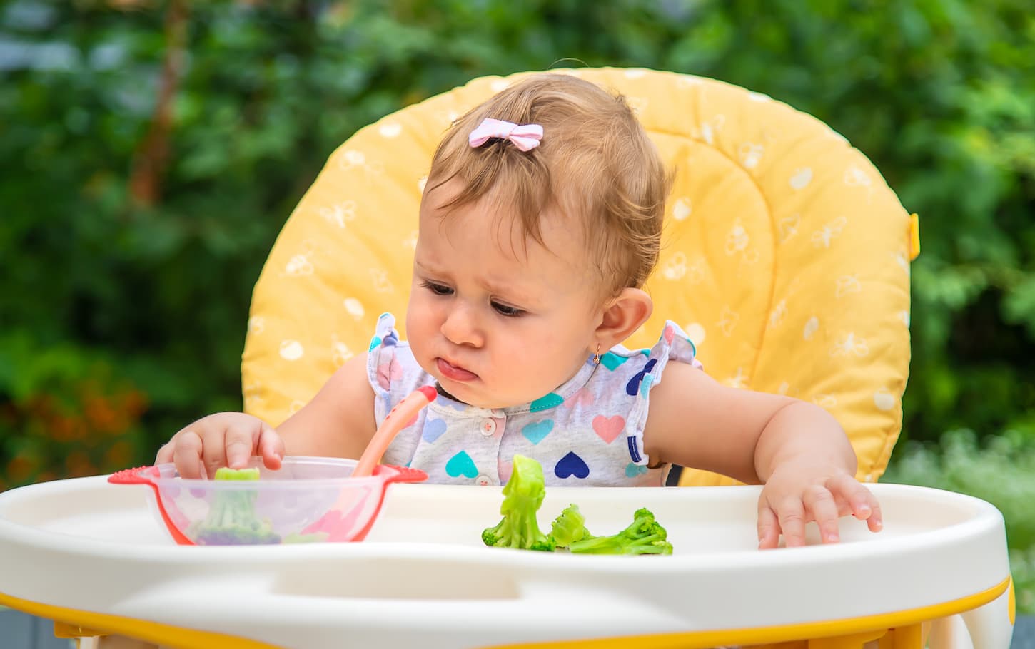 An image of Baby eating pieces of broccoli vegetables.