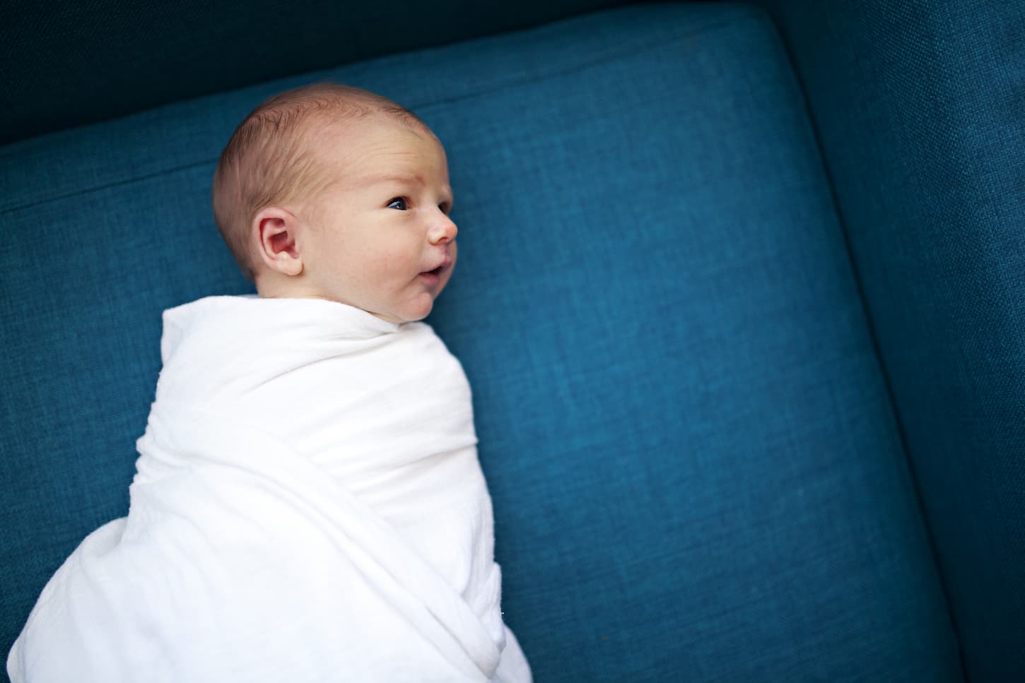 An image of a swaddled newborn baby lying on a blue sofa couch.