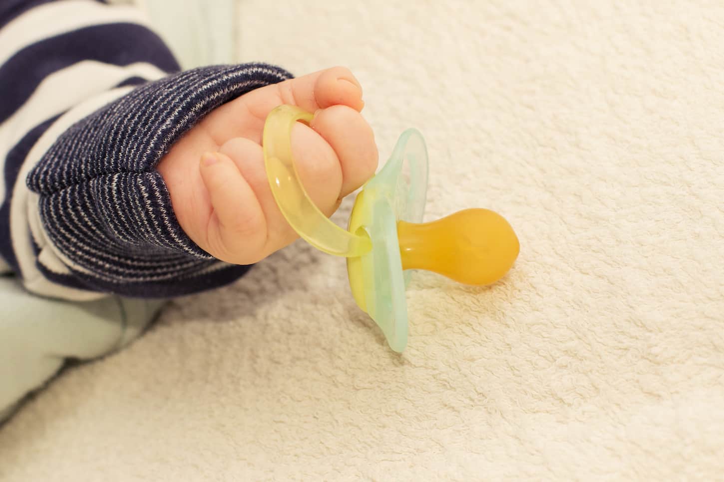 An image of a baby's little hand holding a pacifier.