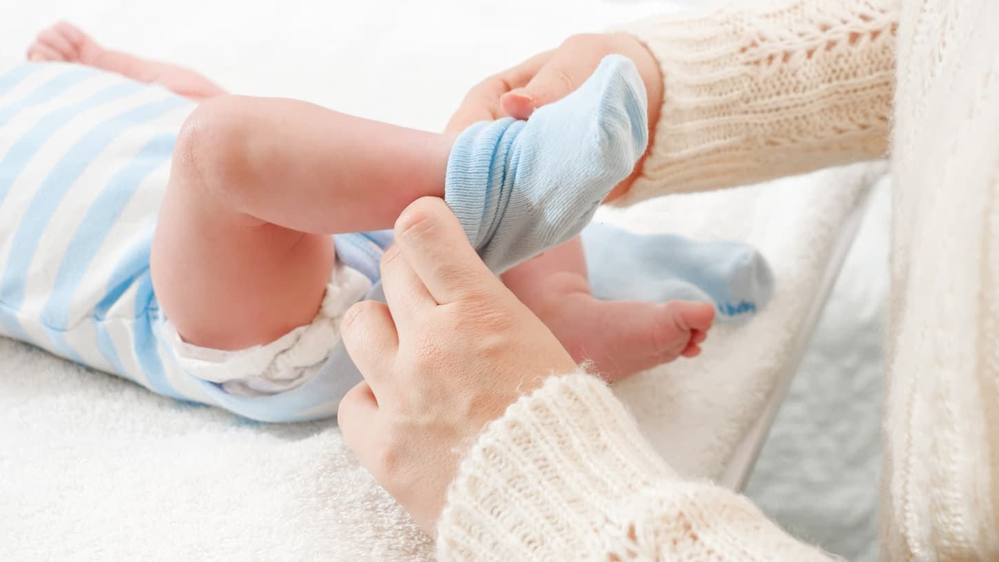 An image of a mother putting on socks on her little baby son lying on changing table.