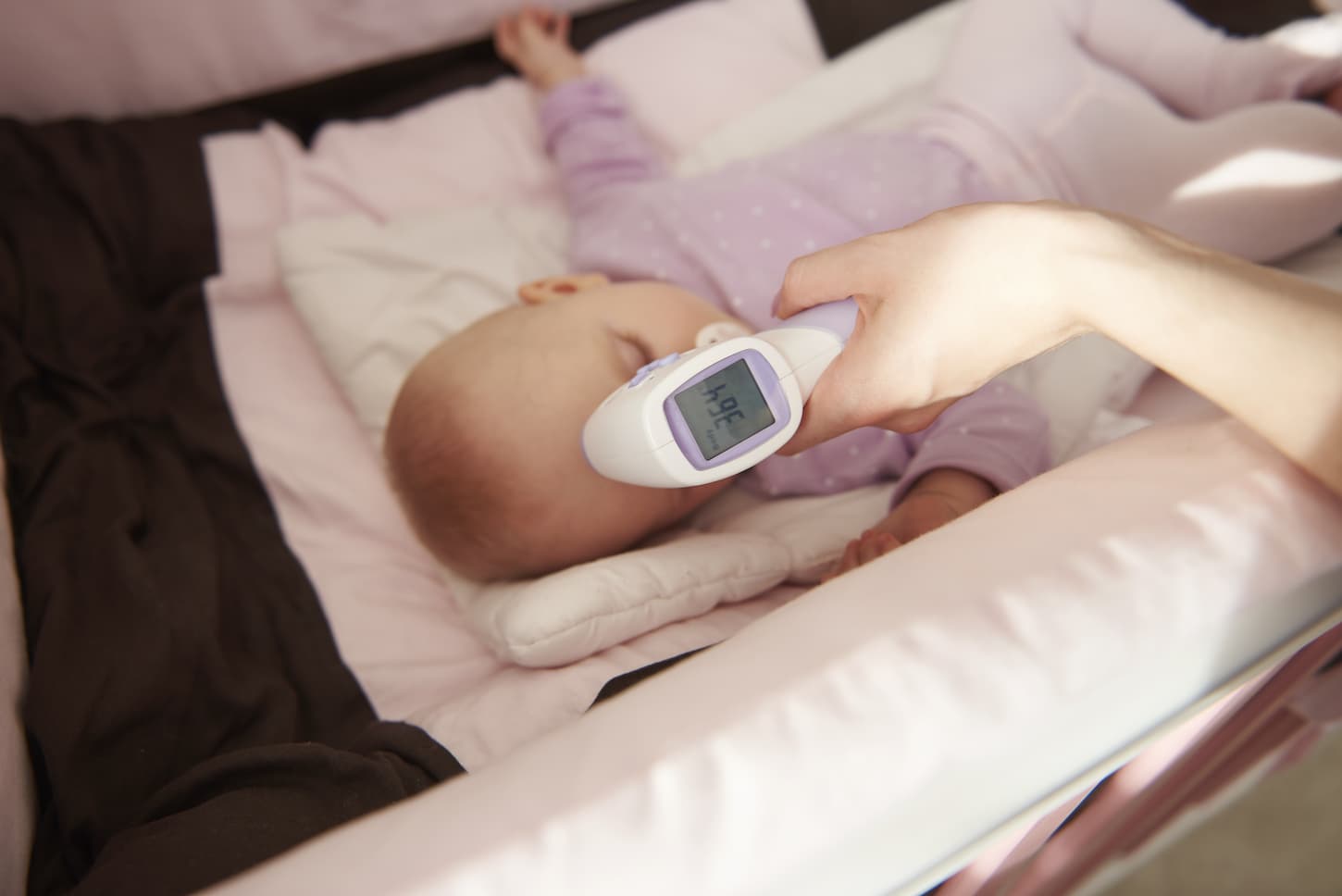An image of a sleeping sick baby with a thermometer focused at the front of the camera.