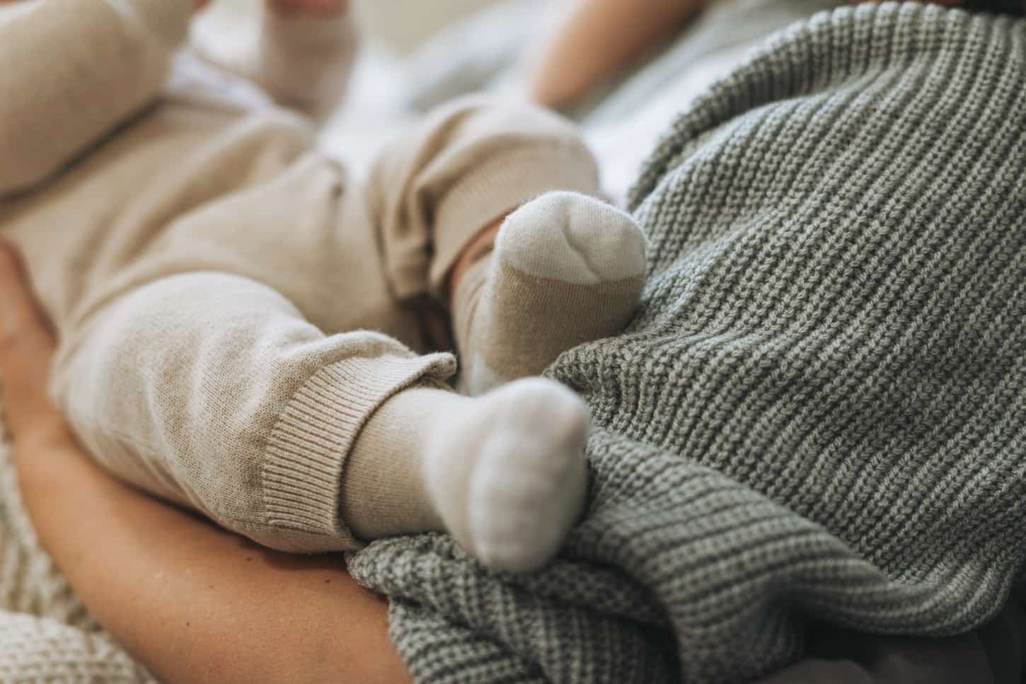 An image of cute baby feet in beige socks, the child with mother on the bed.