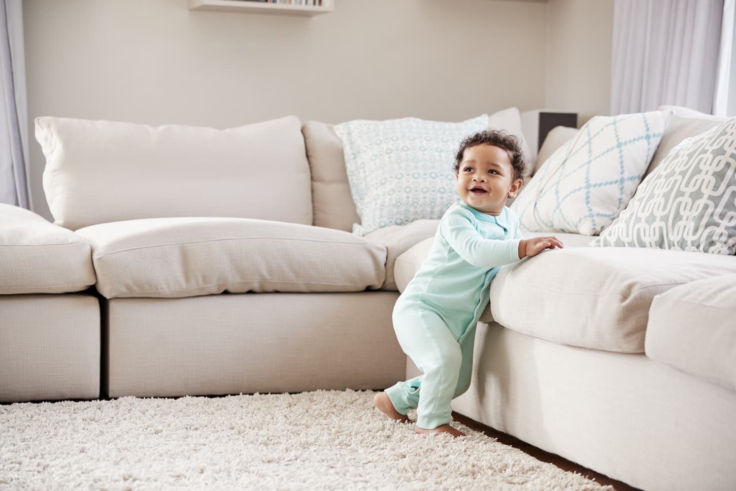 An image of a toddler boy playing in a sitting room with his pastel green sleepsuit.