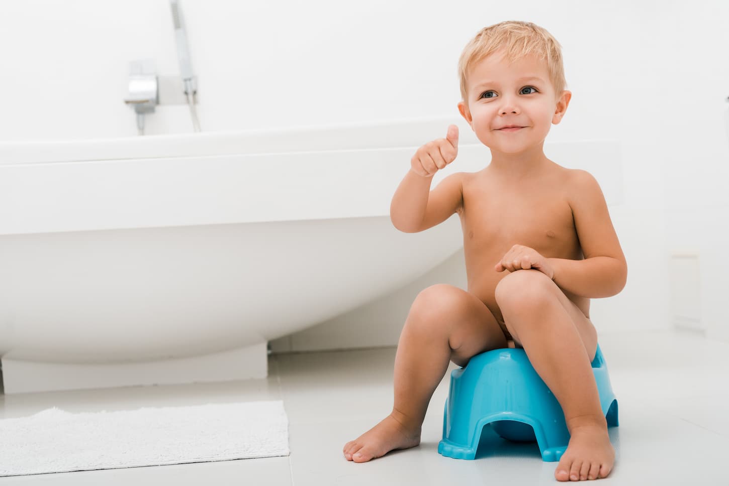 An image of a happy naked toddler boy gesturing while sitting on a blue potty.