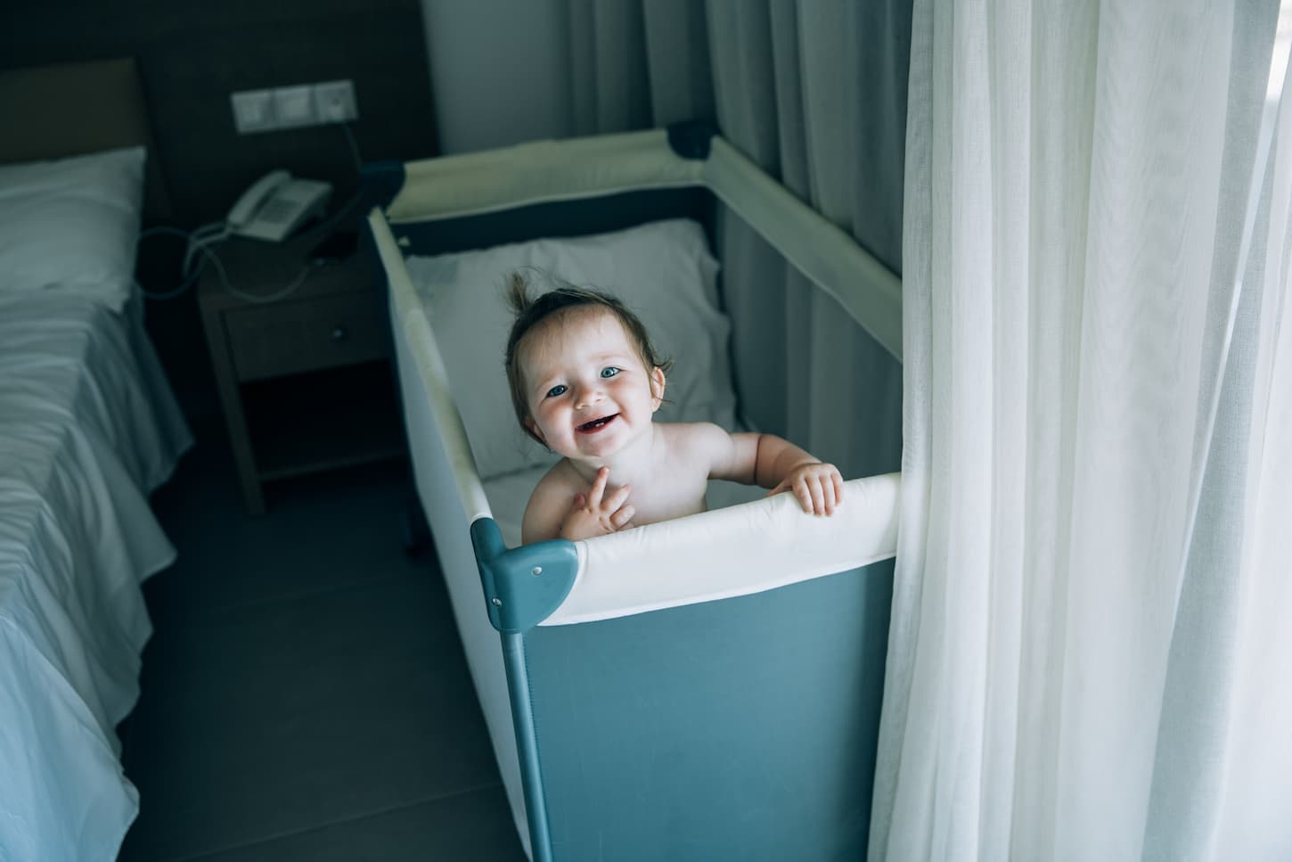 An image of a little baby who just woke up in a good mood and smiling in her crib looking at the camera.