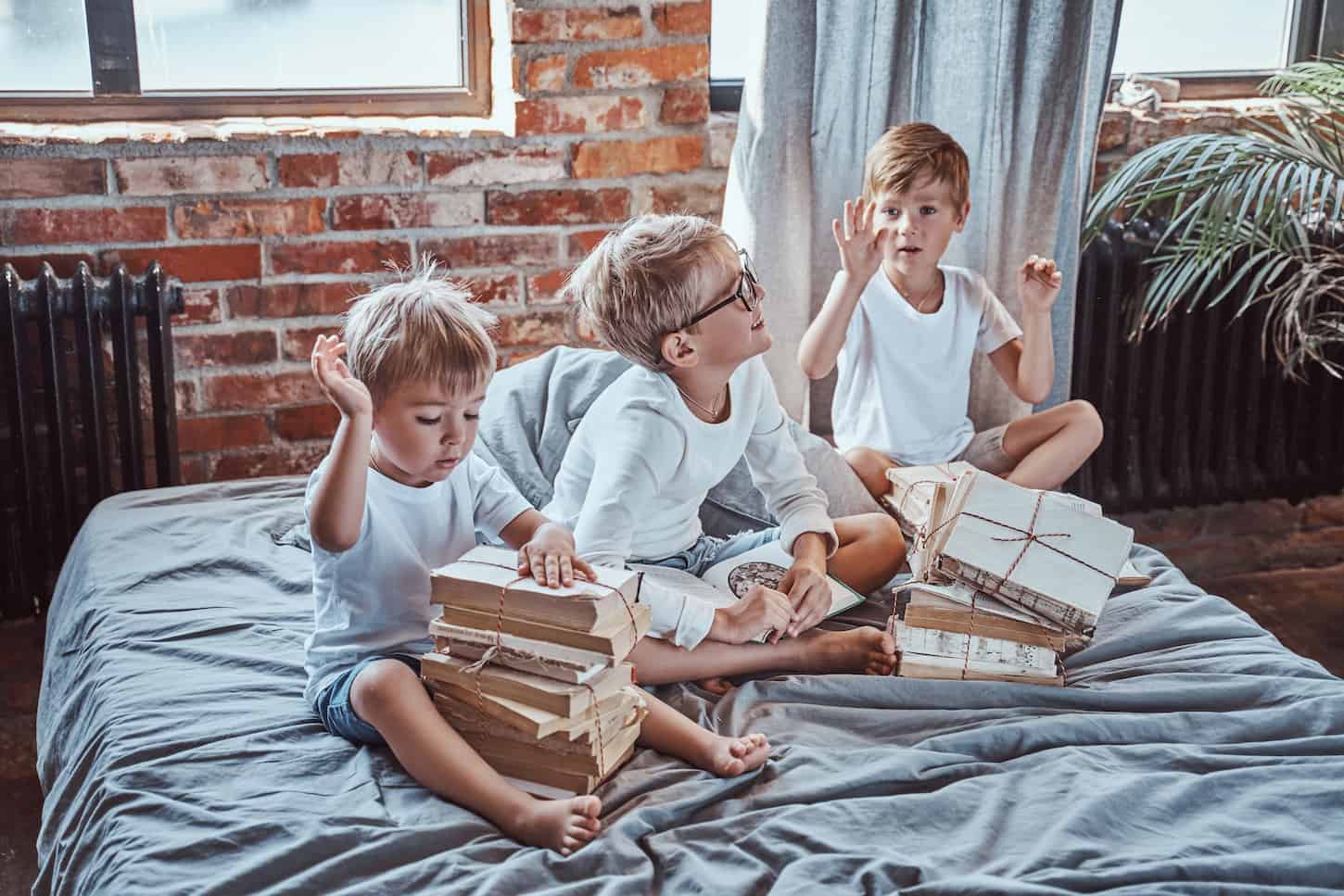 An image of boys after sleep reading books and playing on the soft bed. Preschool brothers getting some knowledge in playschool.