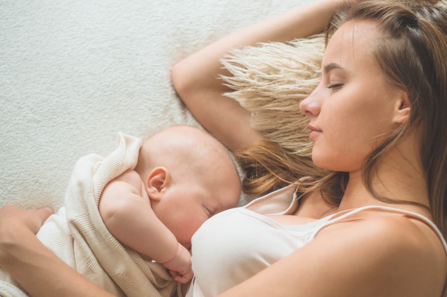 An image of a mom taking a nap while breastfeeding her baby on the bed.