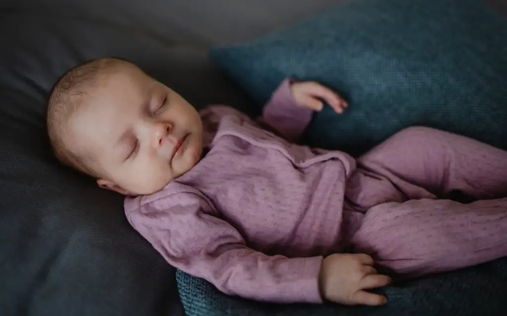 An image of a newborn baby girl, sleeping and lying on sofa indoors at home.