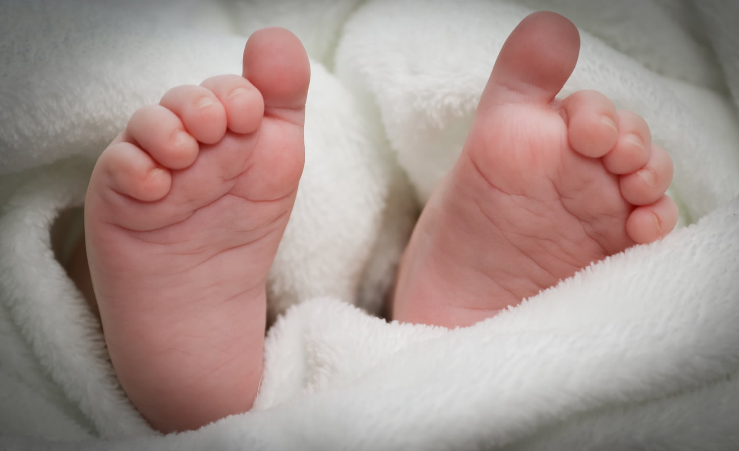 An image of Small feet of a newborn Caucasian baby sticking out of a white fleece blanket.