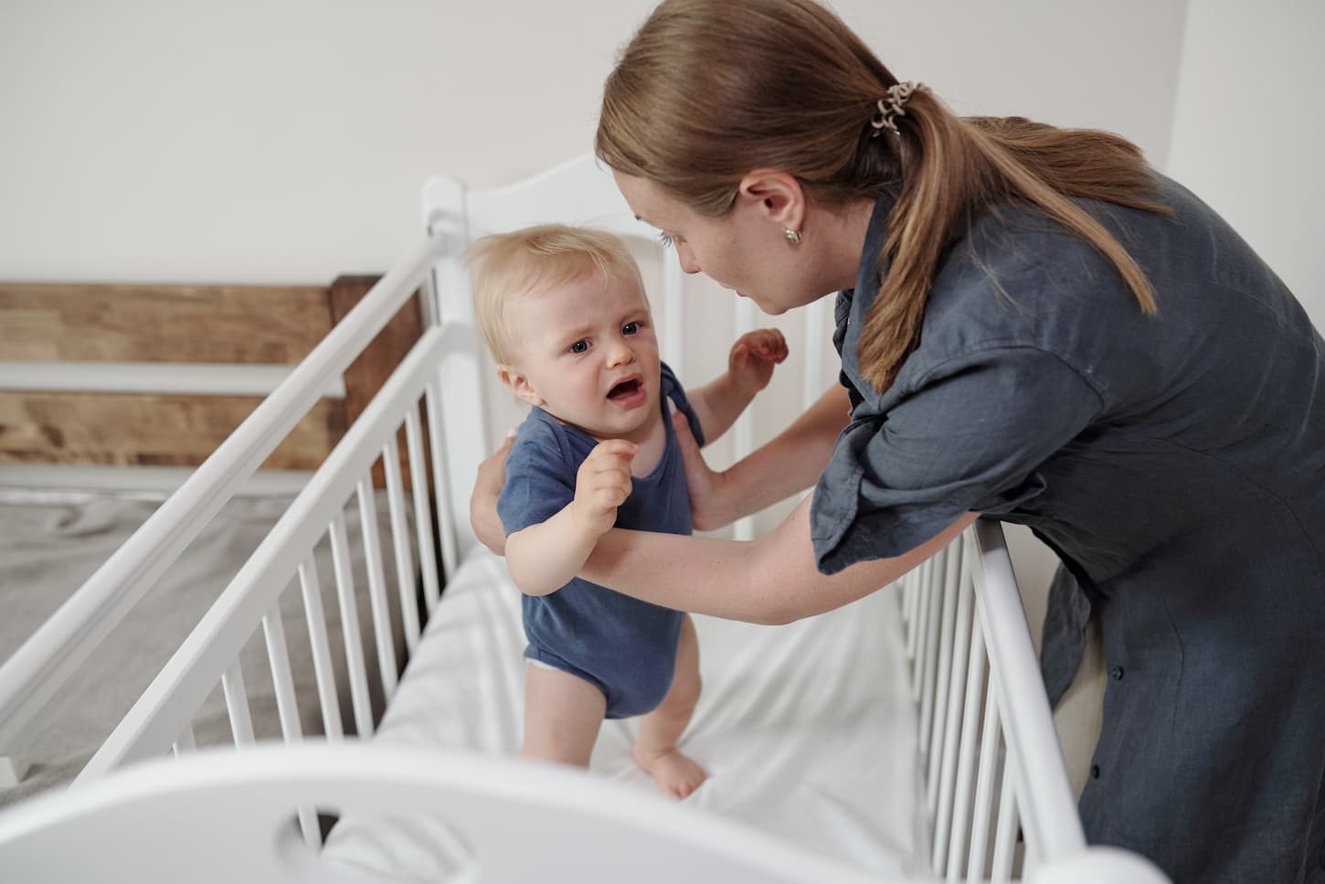 An image of a Young mother with a ponytail taking a frightened baby in her arms from a crib.