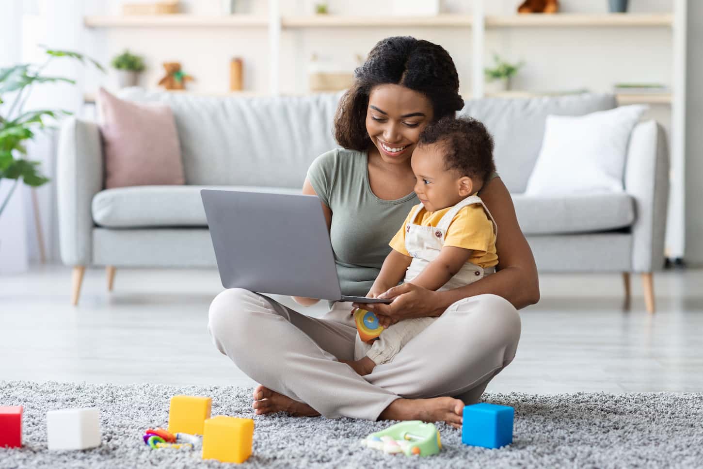 An image of a Young Mom Showing Development Videos On a Laptop To Her Infant Baby At Home, a Happy African American Mother Relaxing With a Little Toddler Child On the Floor In the Living Room, Watching Cartoons Online.