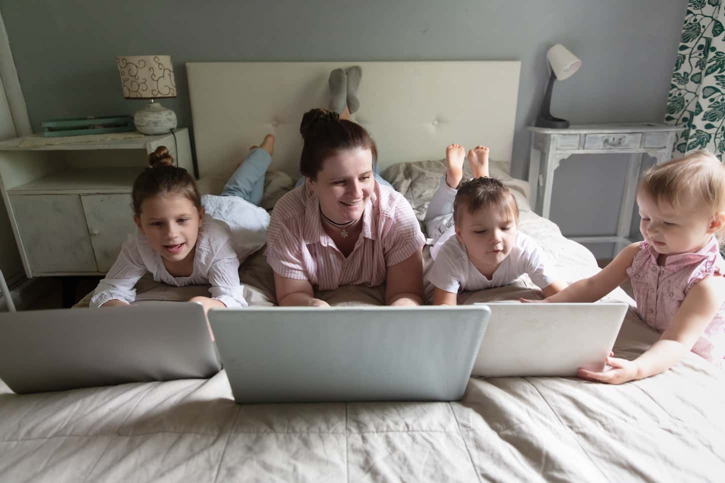An image of a Caucasian Mom and Three children lying in bed with laptops, the concept of online remote work.