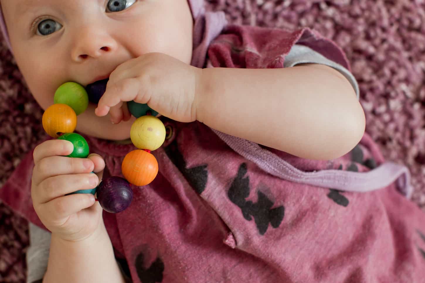 An image of a Baby girl with teething toy in her mouth.