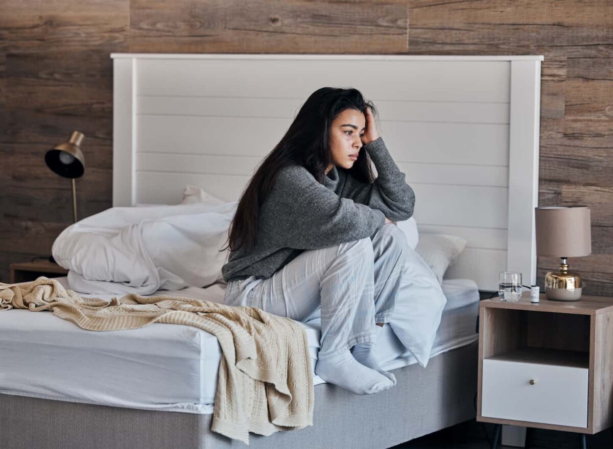 An image of a woman sitting on the side of the bed having anxiety due to insomnia or sleep problems.
